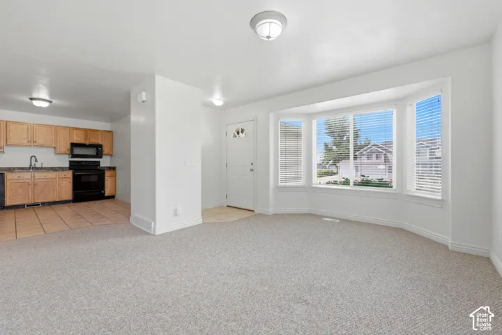 Open concept living space featuring a bay window, light gray carpet, and a kitchen with wood-finish cabinetry, dark countertops, and tile flooring