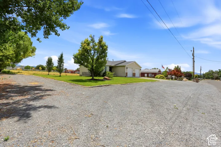 Gravel driveway with ample parking space, bordered by a manicured lawn and mature trees