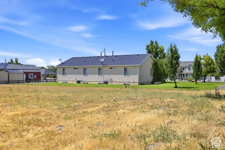 Expansive lot featuring a tan siding residence with a dark roof and white trim windows