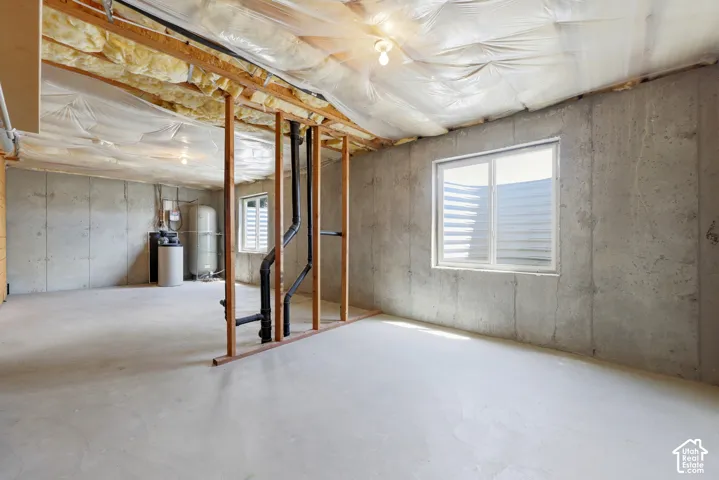 Unfinished lower level featuring concrete walls and flooring, exposed ceiling joists with insulation, a single window, and visible plumbing
