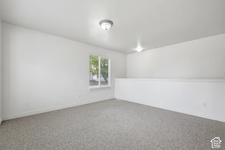 Carpeted loft area featuring a window with blinds, white walls, white baseboards, and two ceiling-mounted light fixtures