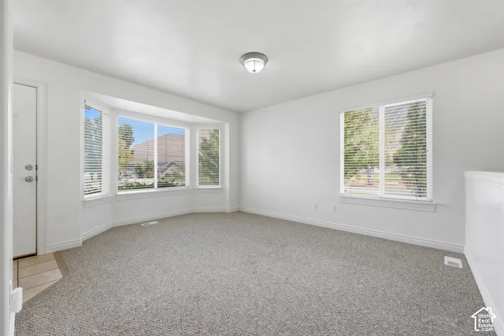 Living area featuring a bay window, additional window with blinds, neutral carpet flooring, and a flush-mount ceiling light fixture