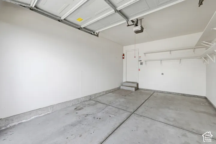 Attached two-car garage featuring a concrete floor, white painted walls, and built-in shelving