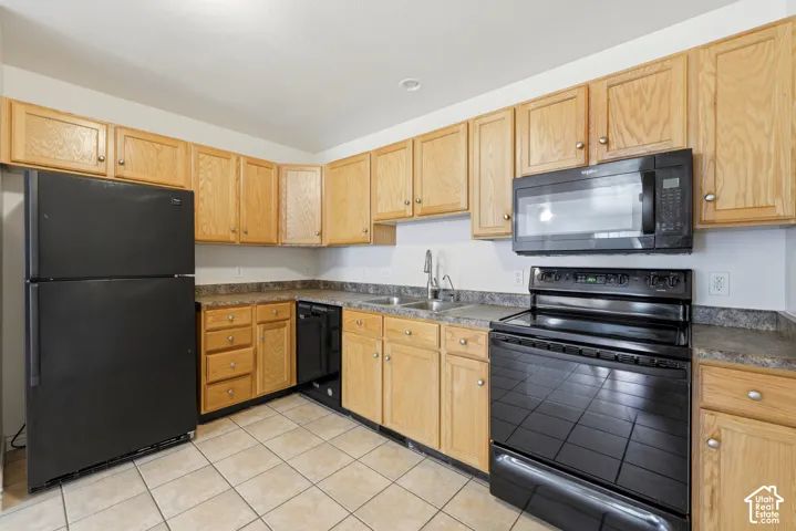 Kitchen featuring light wood cabinetry, dark countertops, and black appliances including a refrigerator, range, and microwave