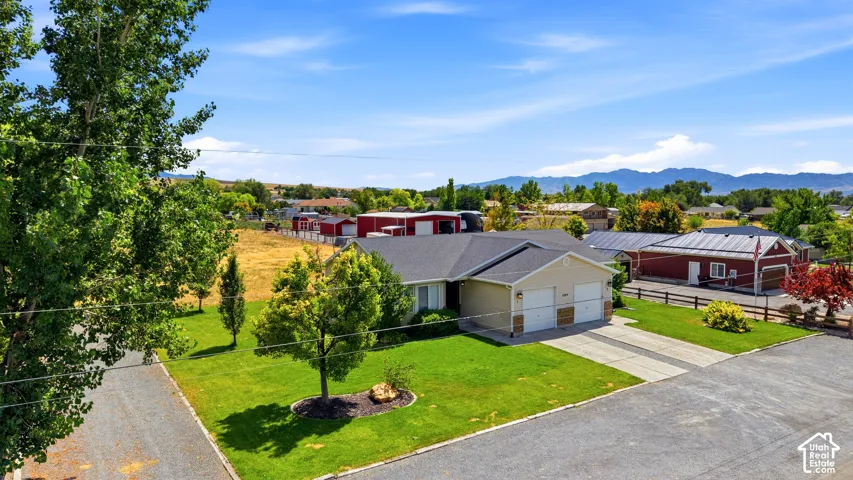 Ranch-style residence featuring a two-car garage, concrete driveway, and a verdant lawn with mature trees