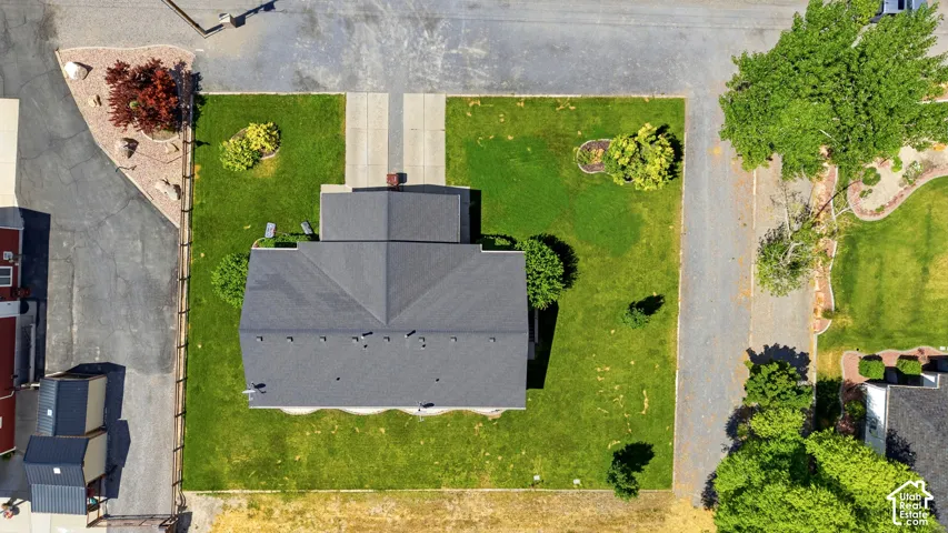 Aerial perspective showcasing a property with a dark shingle roof, green lawn, and concrete driveway
