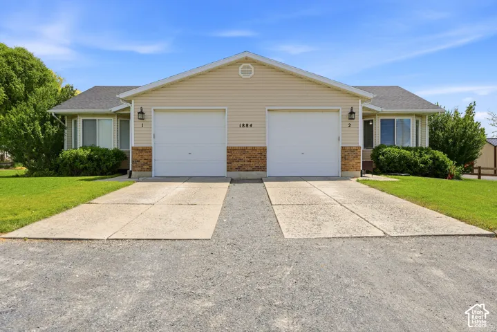 Duplex exterior featuring light-toned siding, brick accents, two single-car garages, and individual concrete driveways