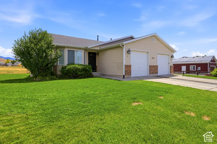 Ranch-style exterior featuring a two-car garage, beige siding, stone accents, a dark entry door, and a green lawn