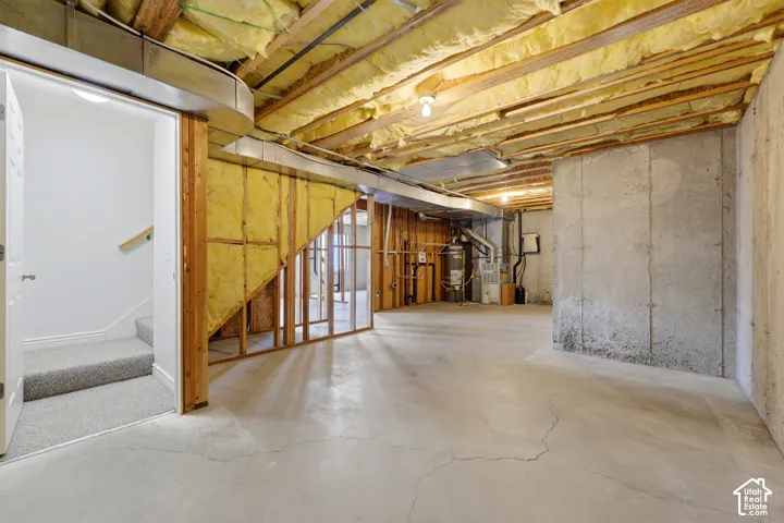 Unfinished basement featuring exposed ceiling joists with insulation, concrete flooring, concrete foundation walls, a framed wall section, and access to a carpeted staircase