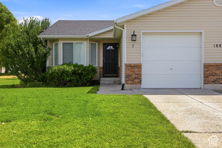 Exterior featuring beige horizontal siding, a red brick facade, an attached single-car garage with a white garage door, a black entry door, and a manicured lawn