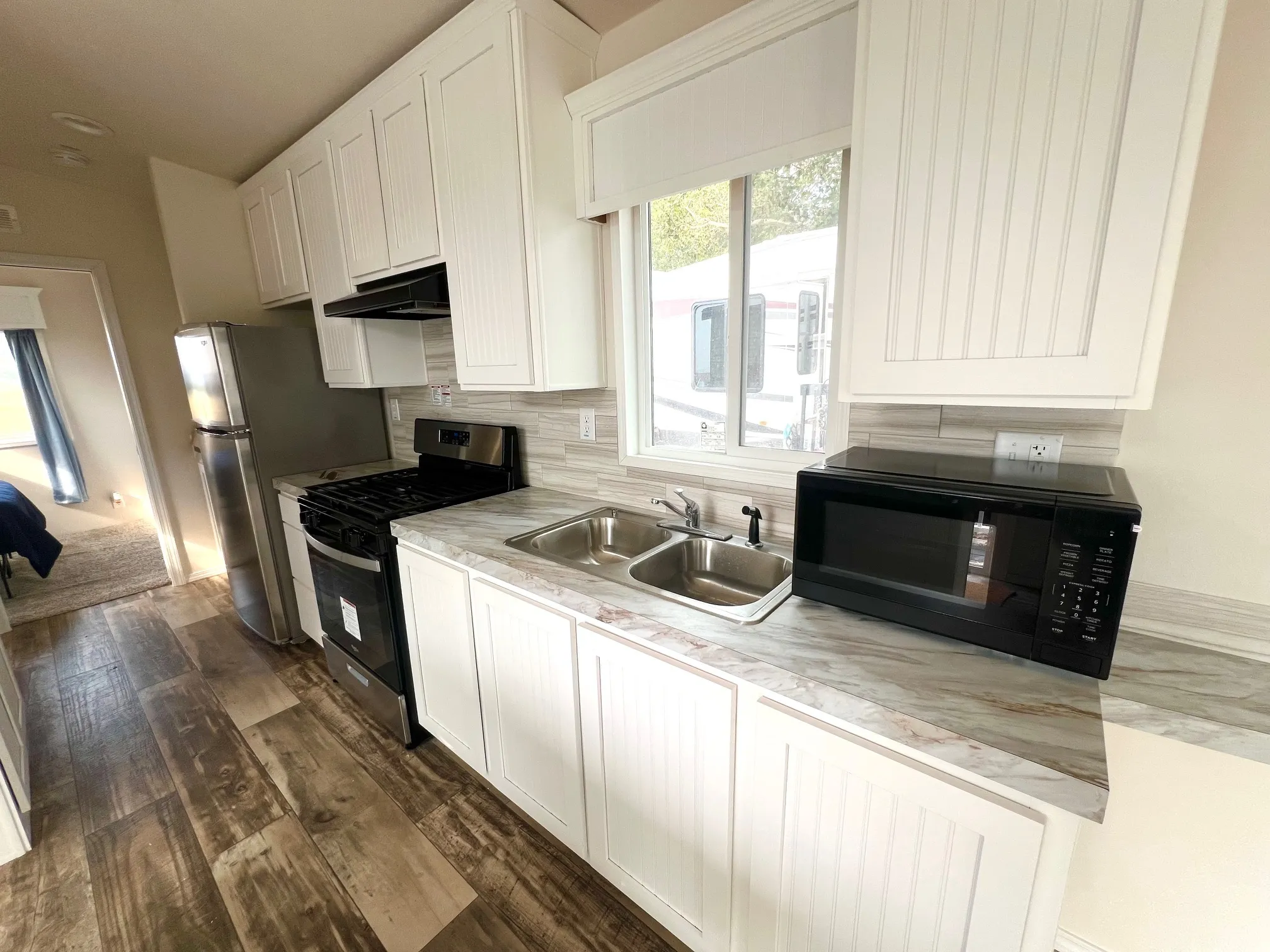 Compact kitchen featuring wood-finish flooring, white cabinetry, stainless steel appliances, a dual basin sink, and a tiled backsplash