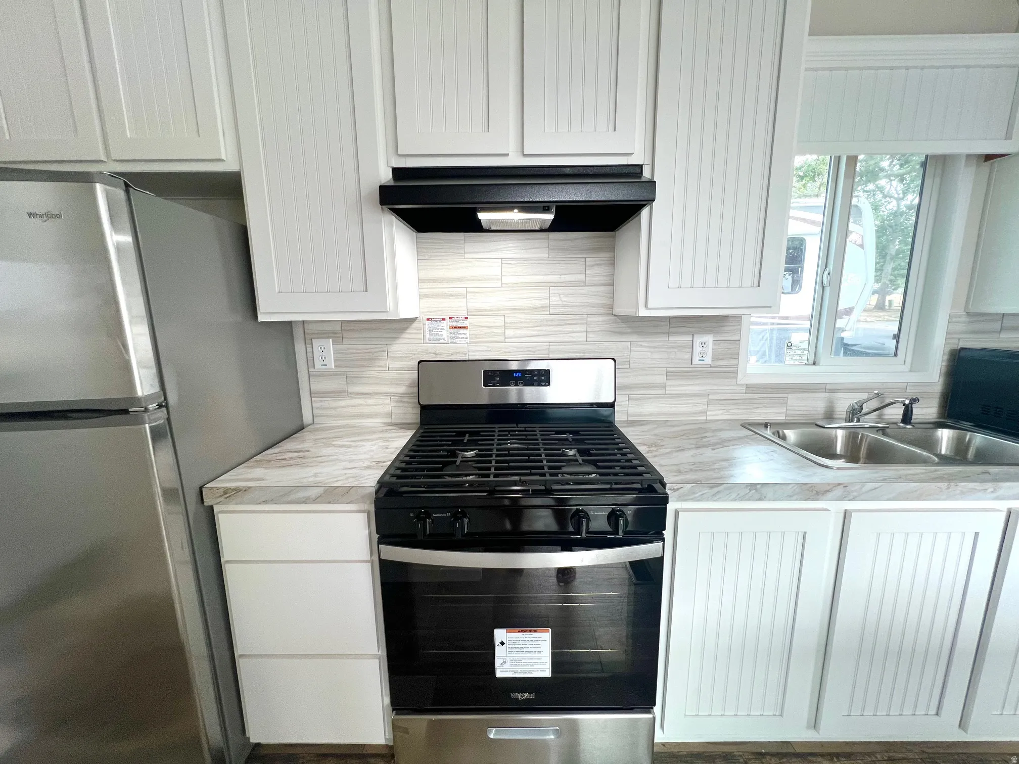 Kitchen featuring a stainless steel range, white shaker-style cabinetry, light-toned backsplash, stainless steel refrigerator, and a double basin sink