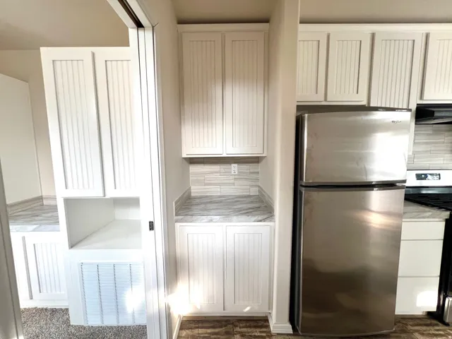 Kitchen area featuring white cabinetry with beadboard paneling, light-toned countertops, a stainless steel refrigerator, and a tiled backsplash