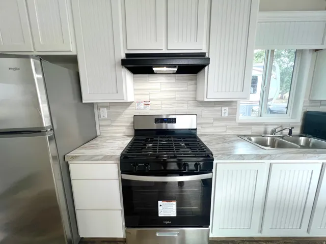 Kitchen featuring a stainless steel range, white shaker-style cabinetry, light-toned backsplash, stainless steel refrigerator, and a double basin sink