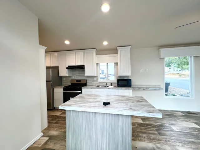 Kitchen featuring an island with a light wood-finish base and a light-toned countertop, white cabinetry, stainless steel refrigerator, black gas range, and a tile backsplash