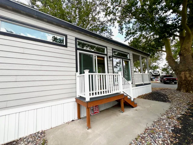 Contemporary manufactured home featuring light gray siding, dark trim windows, and a covered porch