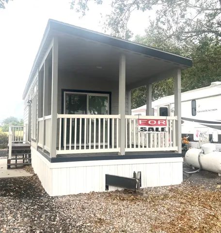 Compact residence featuring a covered front porch with white railings, light gray siding, and an exterior side staircase with dark risers