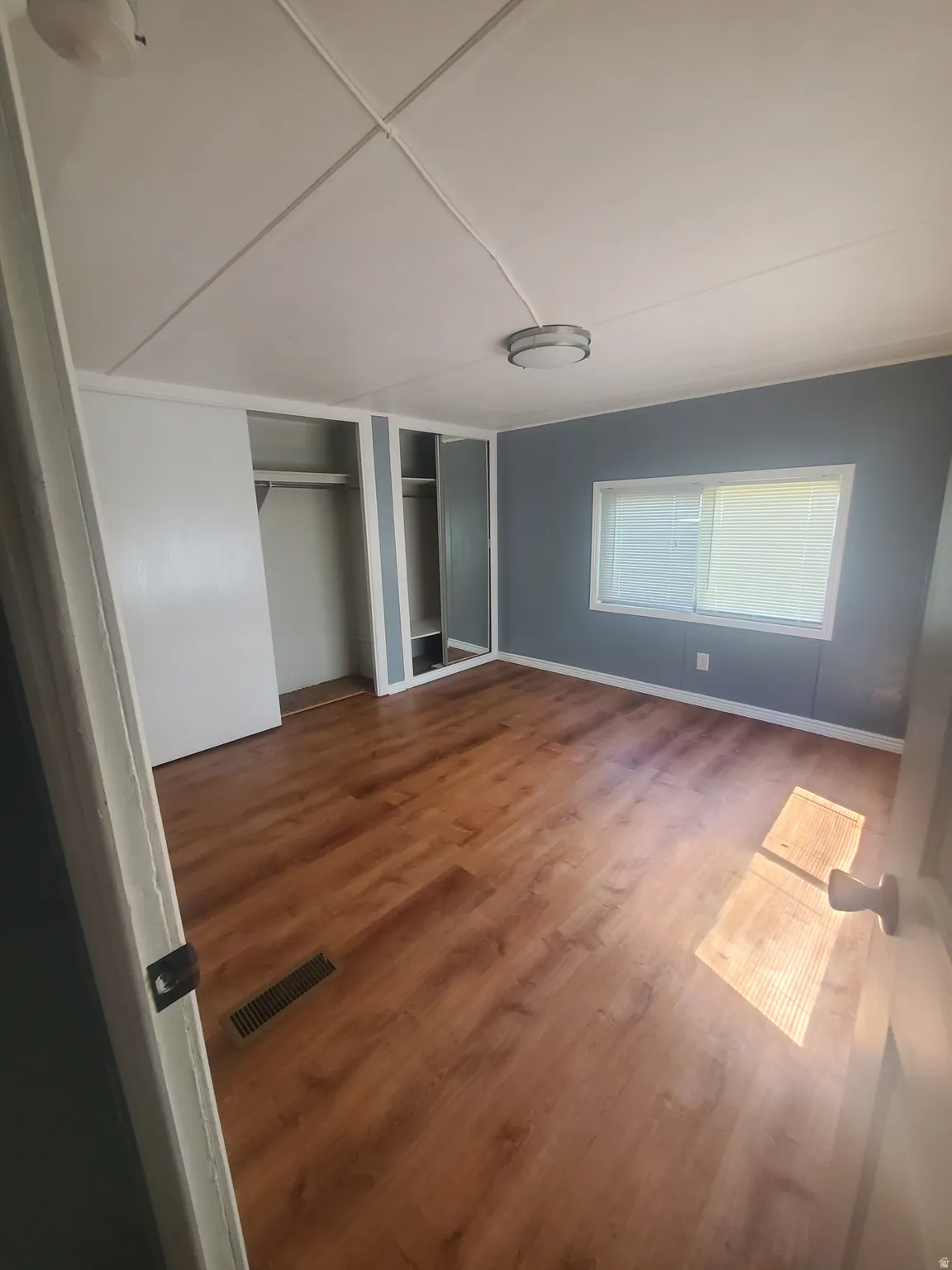 Room featuring wood-finish flooring, two ceiling-mounted light fixtures, a window with horizontal blinds, and a built-in closet with sliding doors