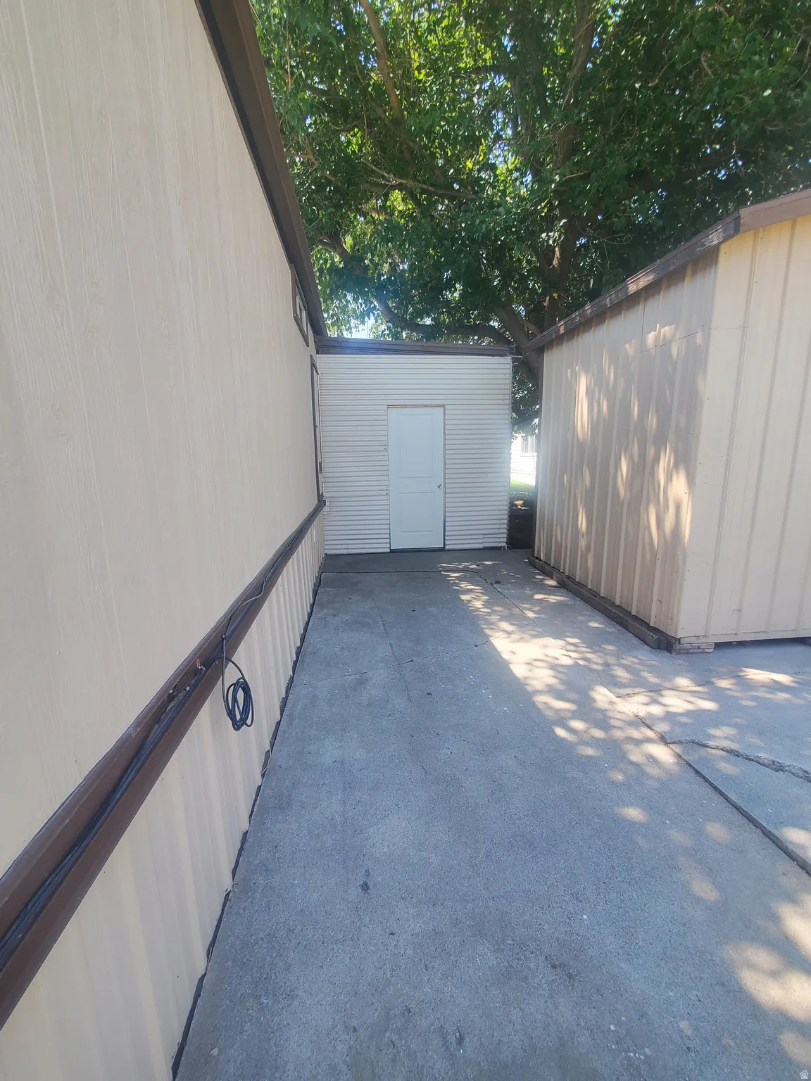 Outdoor concrete walkway between two structures, featuring a central white utility door on a textured wall