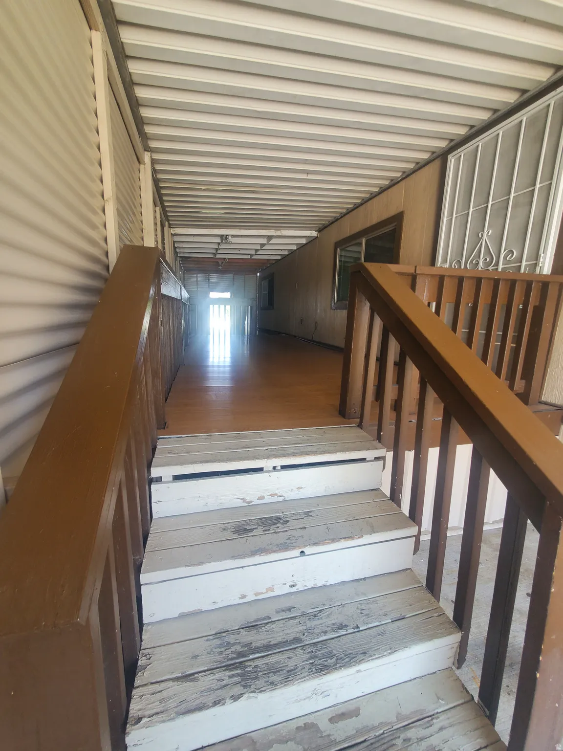 Covered walkway featuring wood-finish flooring, white corrugated metal walls, and a white slat ceiling