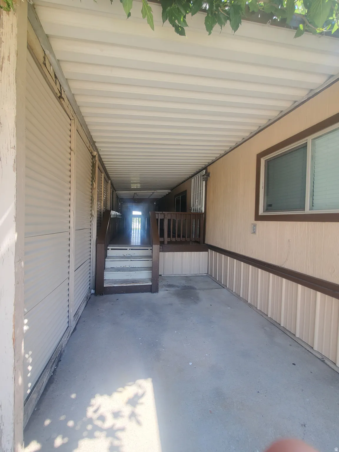 Covered outdoor walkway featuring a concrete surface, a built-in wooden deck with railing, and steps