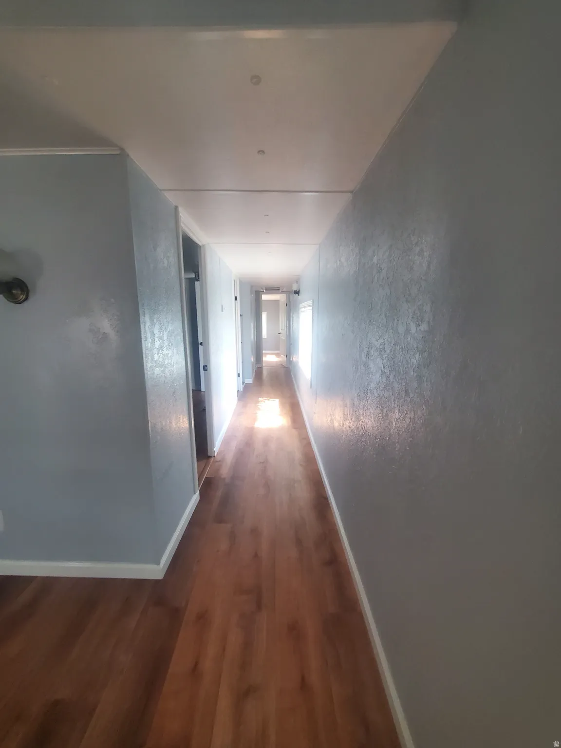 Extended hallway featuring wood-finish flooring, light blue wall paint, white trim, and recessed ceiling lights