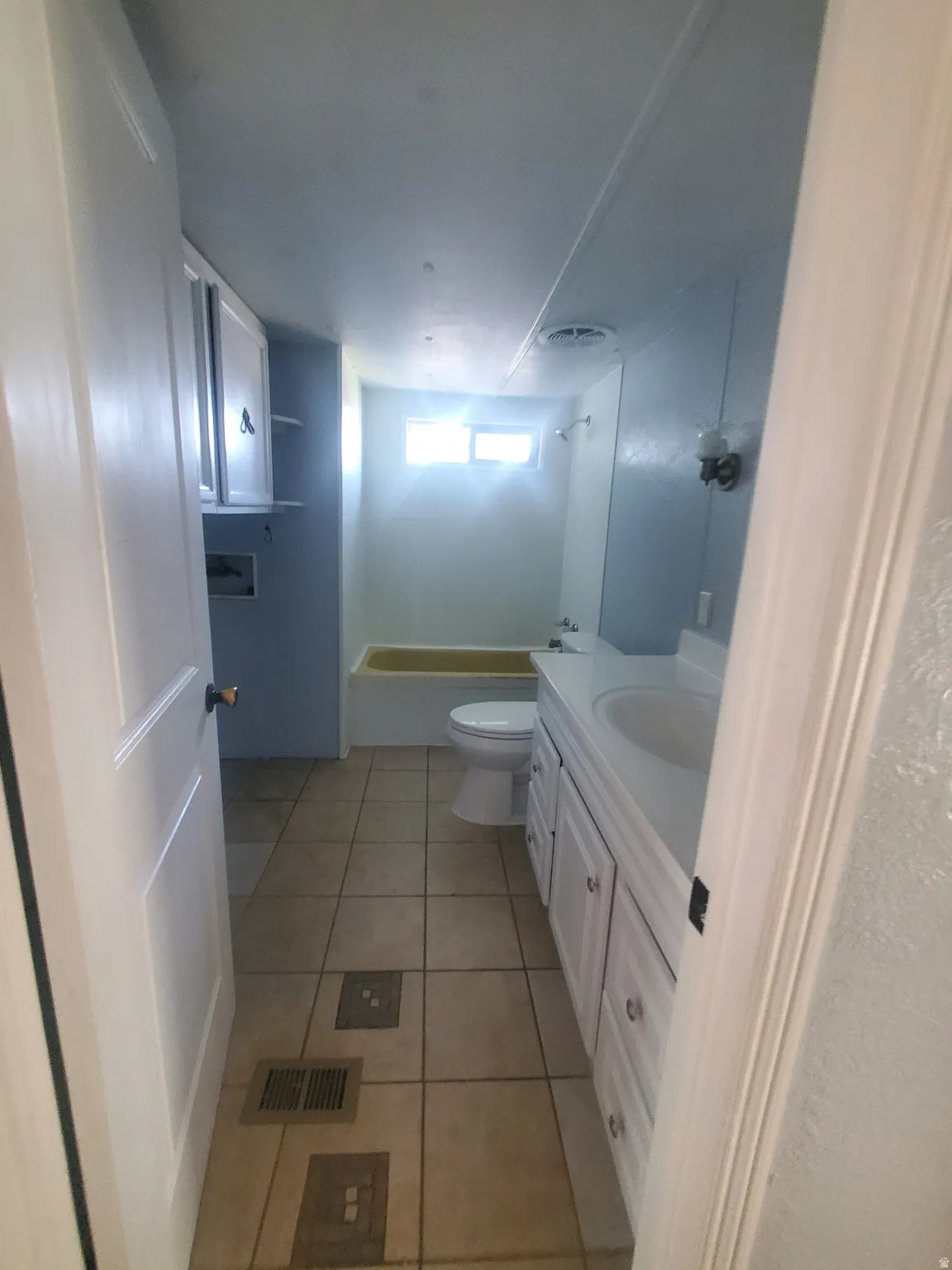 Bathroom featuring a vanity with integrated sink, white cabinetry, tile flooring, and a window