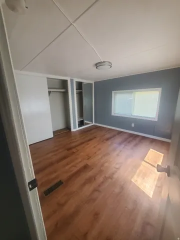 Room featuring wood-finish flooring, two ceiling-mounted light fixtures, a window with horizontal blinds, and a built-in closet with sliding doors