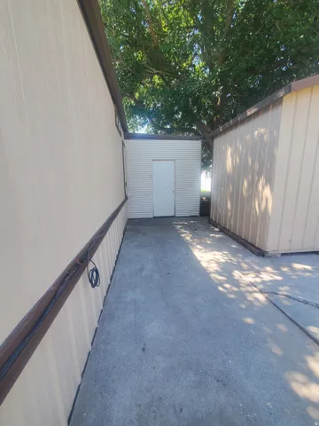 Outdoor concrete walkway between two structures, featuring a central white utility door on a textured wall