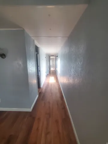 Extended hallway featuring wood-finish flooring, light blue wall paint, white trim, and recessed ceiling lights