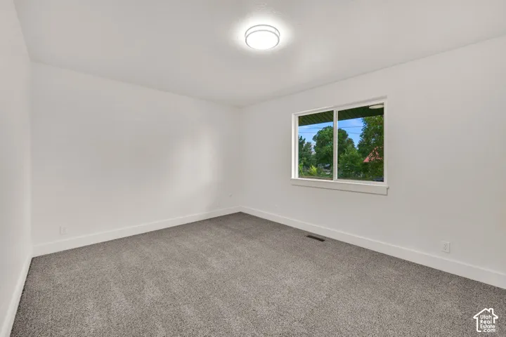Spacious room featuring gray carpet, bright white walls, a large window with white trim, and a flush-mount ceiling light