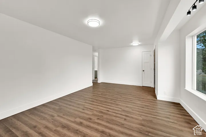 Spacious interior room featuring wood-finish flooring, white baseboards, and a large window with exterior scenery