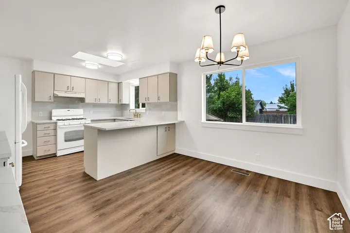Open-concept kitchen and dining area featuring wood-finish flooring, white appliances, light-colored cabinetry, quartz countertops, and a modern chandelier