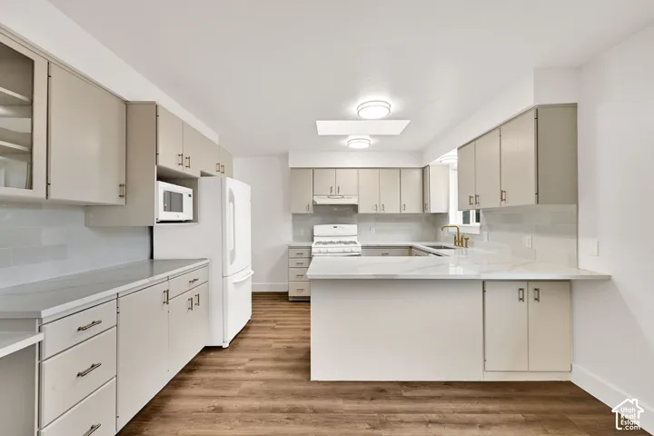 Kitchen featuring wood-finish flooring, a white subway tile backsplash, light cabinetry, and light countertops