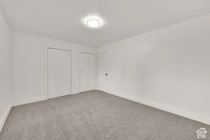 Carpeted room with white walls, two bi-fold panel doors, a single panel door, and a flush mount ceiling light fixture