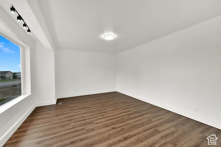 Spacious room featuring wood-finish flooring, white walls, and bright overhead lighting