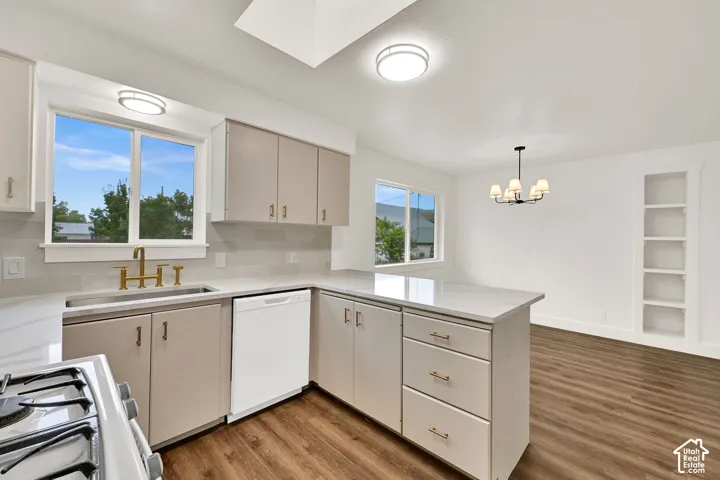 Open-concept kitchen featuring light-toned cabinetry, a corner sink with a brass-finish faucet, white countertops, and a white dishwasher