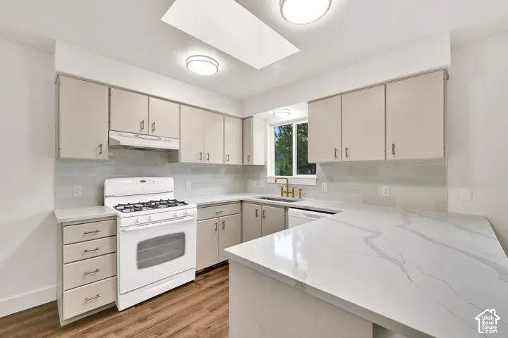 Spacious kitchen featuring white cabinetry, quartz countertops, subway tile backsplash, wood-finish flooring, and a skylight