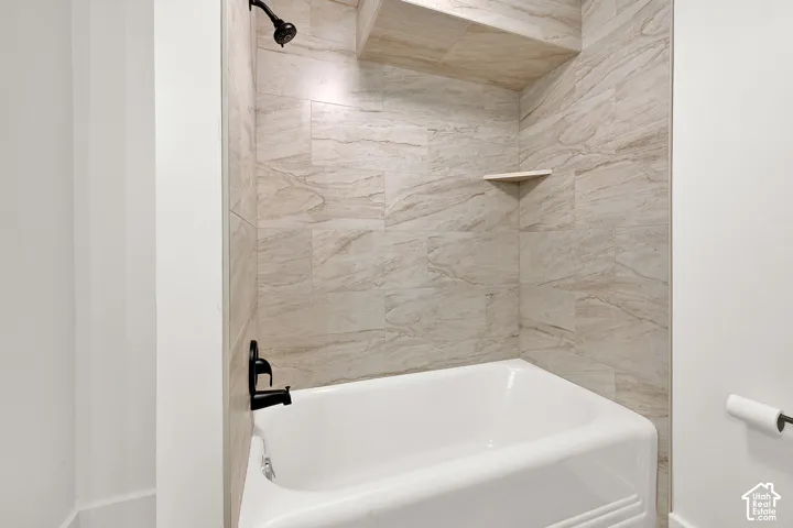 Bathtub and shower combination featuring neutral-toned rectangular wall tiling, a built-in shower shelf, a recessed storage niche, and matte black fixtures