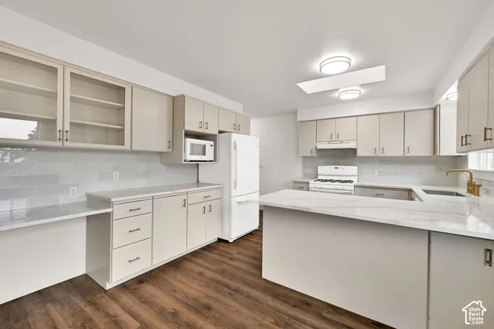 Contemporary kitchen featuring light wood-finish cabinetry, quartz countertops, a subway tile backsplash, a central island with an undermount sink and brass-finish faucet, and wood-finish flooring
