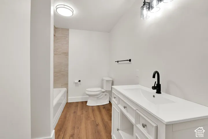 Bathroom featuring a white vanity with integrated sink, matte black faucet, and wood-finish flooring
