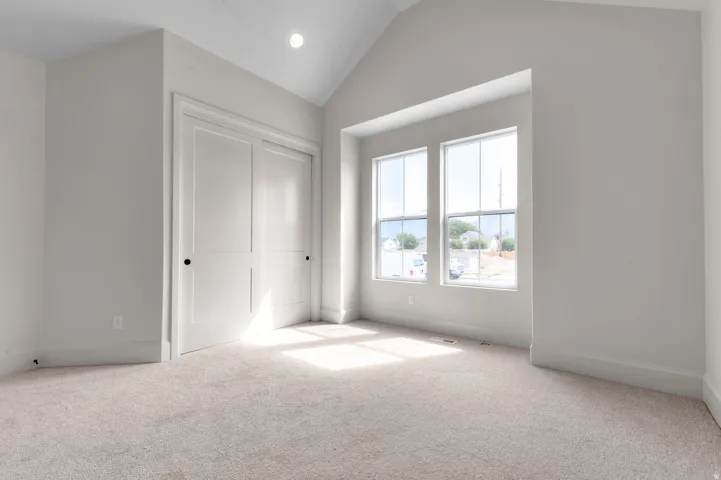 Vaulted ceiling room featuring light-toned carpeting and neutral wall tones