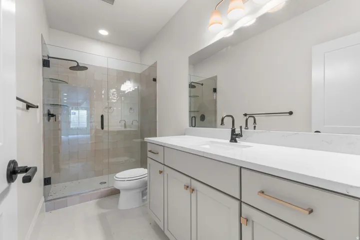 Bathroom featuring a frameless glass shower enclosure, a dual-sink vanity with a light countertop, a rectangular mirror, and matte black fixtures