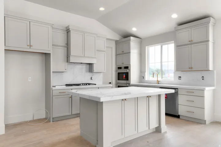 Kitchen featuring light gray cabinetry, a central island with a stone countertop, built-in double ovens, a gas range with a range hood, and recessed lighting