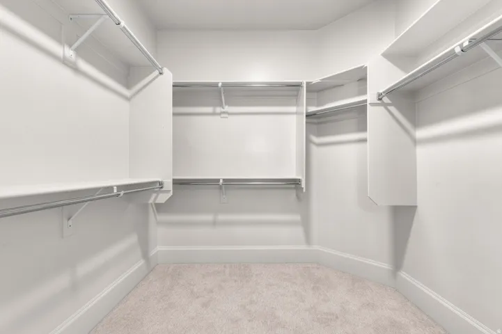 Walk-in closet featuring light-toned carpeting, white walls, and multiple levels of shelving and hanging rods