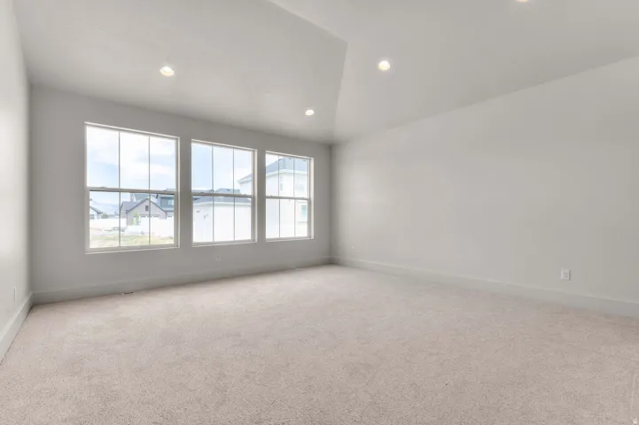 Spacious room featuring three large windows, vaulted ceiling, recessed lighting, neutral wall tones, and light-colored carpeting