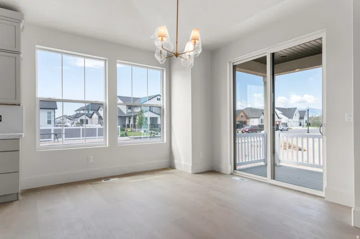 Bright interior space featuring light wood-finish flooring, a contemporary chandelier, two large windows, and a sliding glass door opening to an outdoor deck