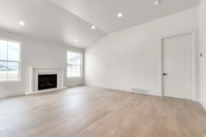 Spacious living area featuring light wood-finish flooring, a white mantel fireplace, and two large windows