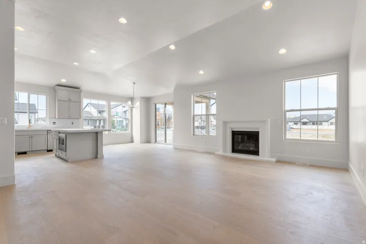 Open-concept living area with light wood-finish flooring, recessed lighting, and a white fireplace