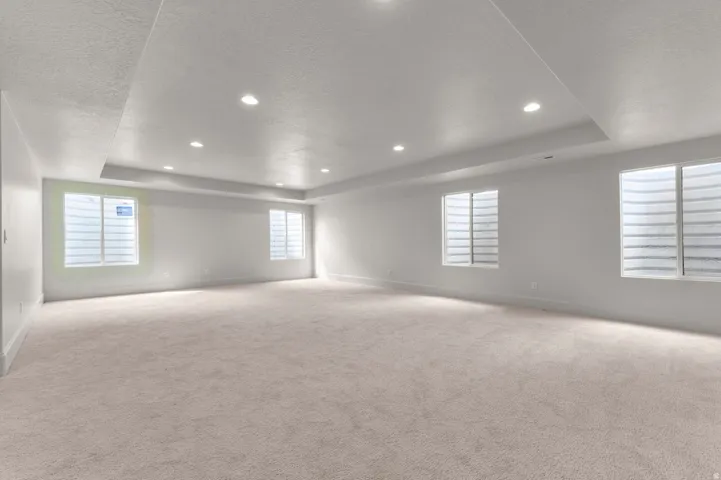 Expansive room featuring light-colored carpeting, multiple windows with white grilles, recessed lighting, and a tray ceiling detail
